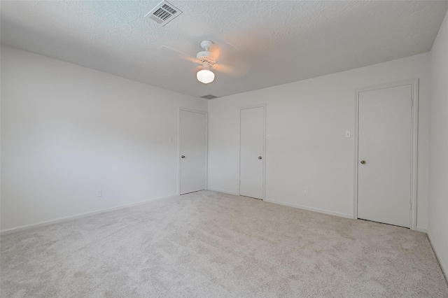 carpeted empty room featuring baseboards, ceiling fan, visible vents, and a textured ceiling