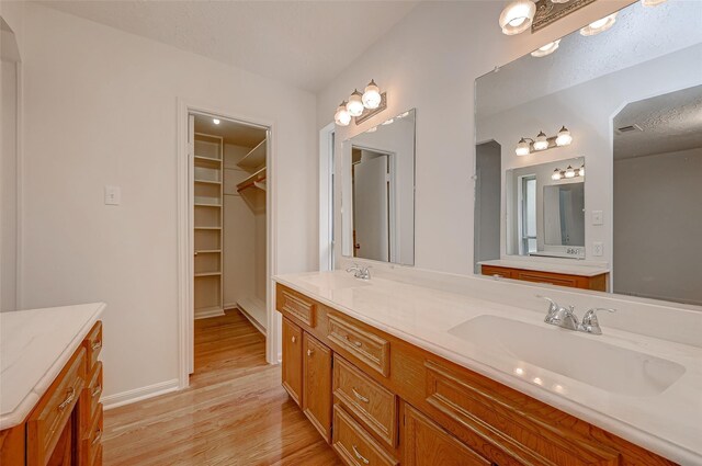 bathroom with double vanity, wood finished floors, a sink, and a walk in closet