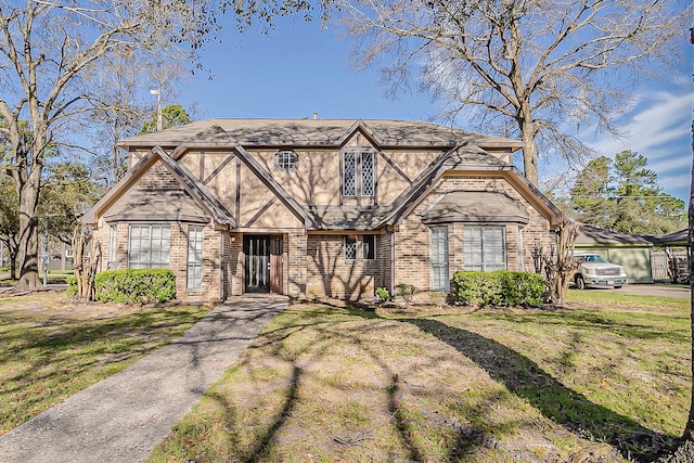 tudor-style house featuring brick siding, a front lawn, and stucco siding