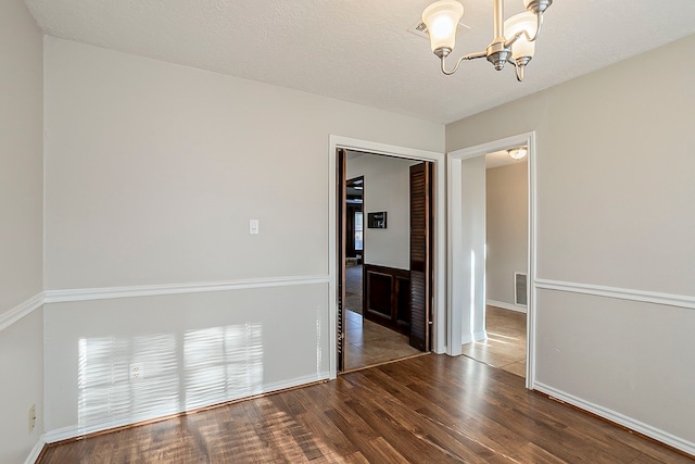 unfurnished room featuring a notable chandelier, visible vents, a textured ceiling, wood finished floors, and baseboards