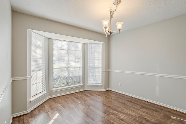 unfurnished room featuring baseboards, wood finished floors, and an inviting chandelier