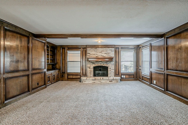 unfurnished living room featuring a textured ceiling, built in shelves, a fireplace, carpet flooring, and beamed ceiling