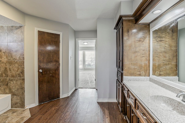 bathroom featuring baseboards, a washtub, wood finished floors, and vanity