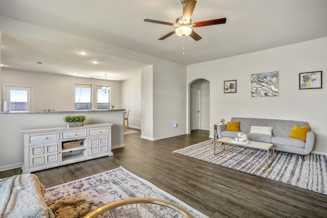 living area featuring a ceiling fan, wood finished floors, arched walkways, and baseboards