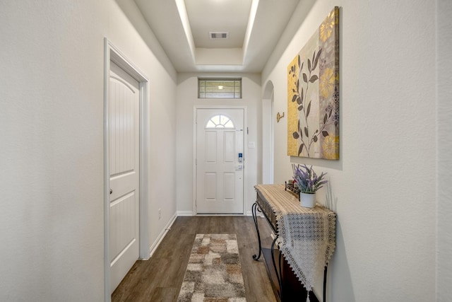 doorway featuring visible vents, baseboards, arched walkways, a raised ceiling, and dark wood-style flooring