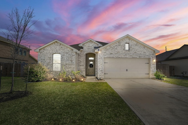 french country home with brick siding, concrete driveway, fence, and a front lawn