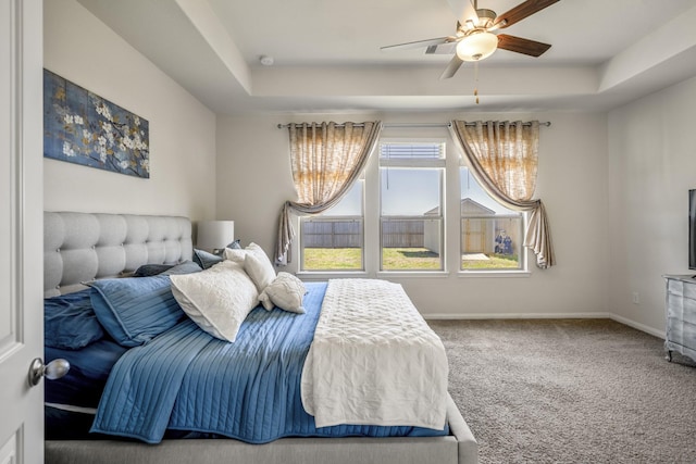 carpeted bedroom with a ceiling fan, a raised ceiling, and baseboards