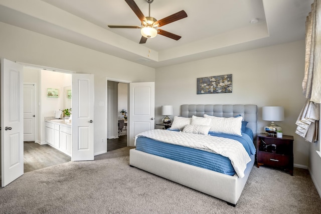 carpeted bedroom featuring baseboards, a raised ceiling, ceiling fan, and ensuite bathroom