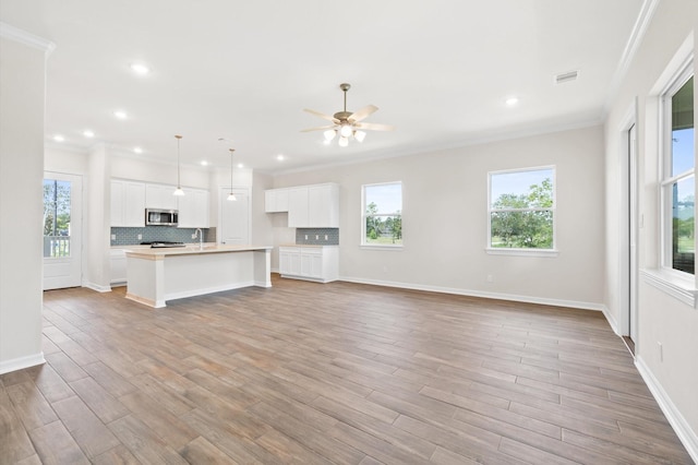 unfurnished living room featuring ornamental molding, light wood finished floors, visible vents, and a healthy amount of sunlight