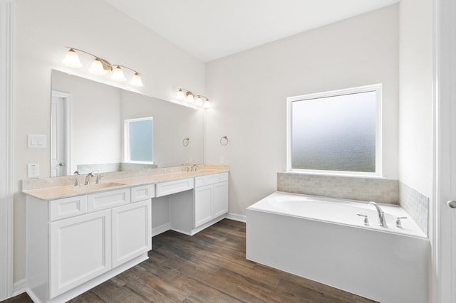 bathroom with double vanity, a garden tub, a sink, and wood finished floors