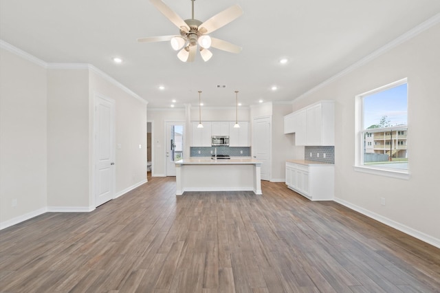 kitchen with stainless steel microwave, backsplash, open floor plan, white cabinets, and wood finished floors