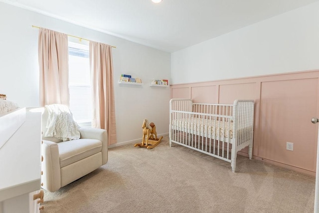 carpeted bedroom with a nursery area, a decorative wall, and wainscoting