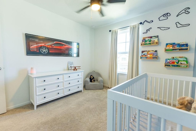 bedroom with a nursery area, ceiling fan, light carpet, and baseboards