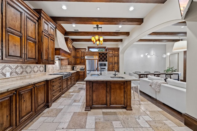 kitchen with built in appliances, custom range hood, stone tile floors, arched walkways, and a sink