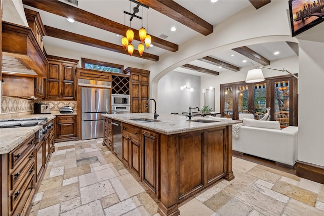 kitchen featuring a sink, built in appliances, arched walkways, and stone tile flooring