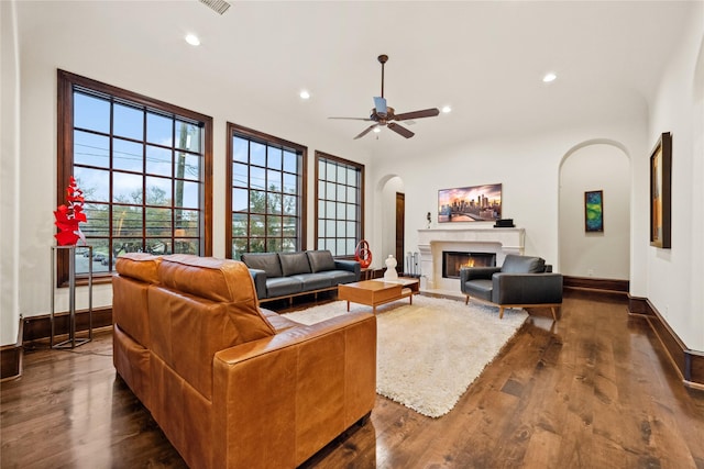 living room with baseboards, dark wood finished floors, recessed lighting, a warm lit fireplace, and arched walkways