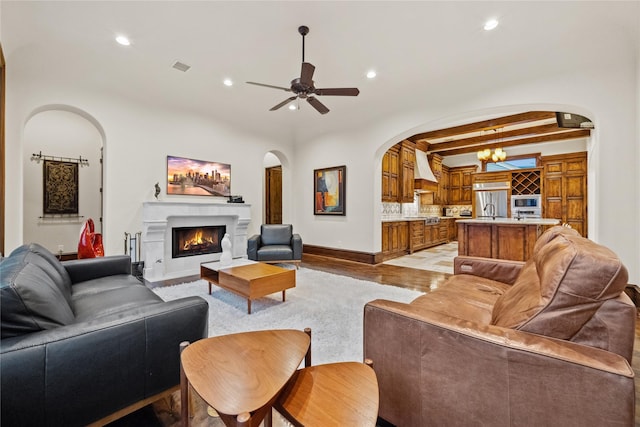 living area with light wood-style floors, recessed lighting, arched walkways, and a lit fireplace