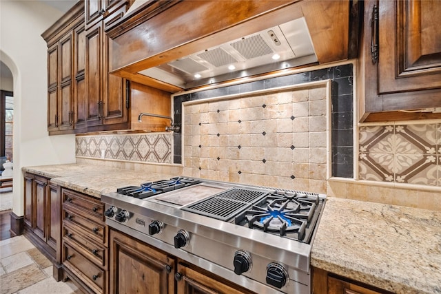 kitchen with arched walkways, stone tile flooring, decorative backsplash, stainless steel gas stovetop, and wall chimney range hood