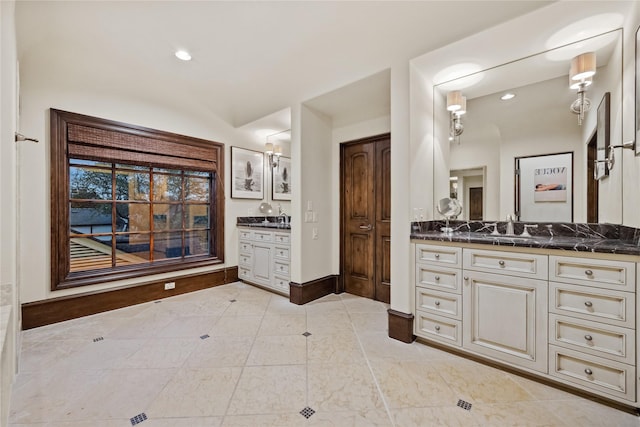 full bath featuring a sink, baseboards, and two vanities