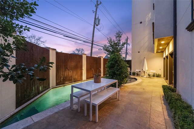 patio terrace at dusk featuring a fenced backyard and outdoor dining space