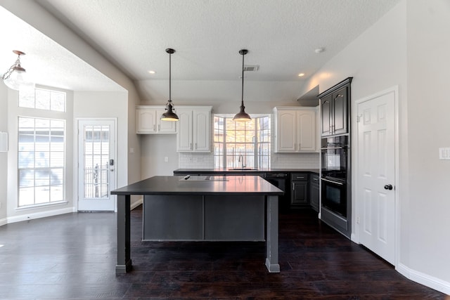 kitchen featuring dark countertops, visible vents, dark wood-type flooring, decorative backsplash, and a sink