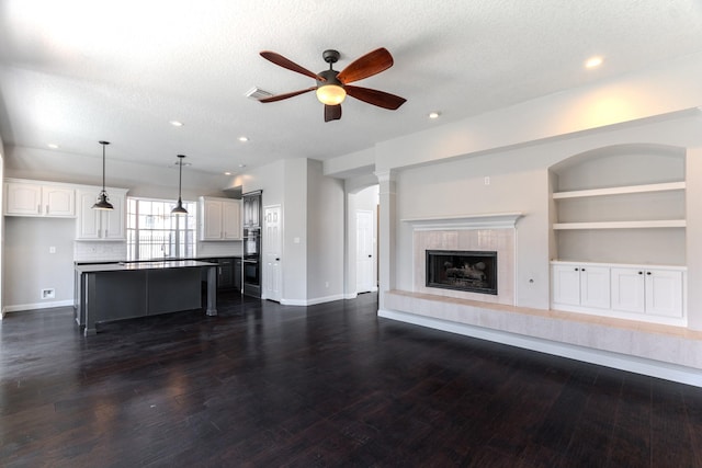 unfurnished living room featuring baseboards, ceiling fan, a tiled fireplace, dark wood finished floors, and a textured ceiling