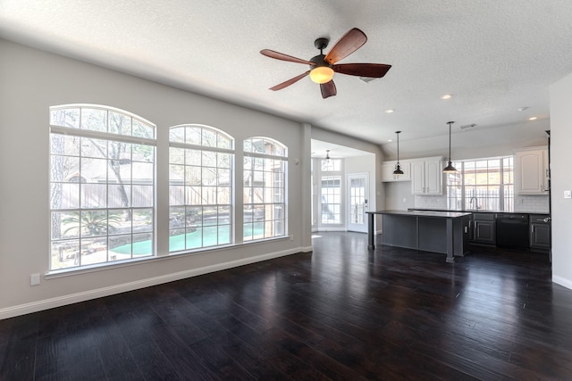 unfurnished living room featuring dark wood-style floors, a ceiling fan, baseboards, and a sink