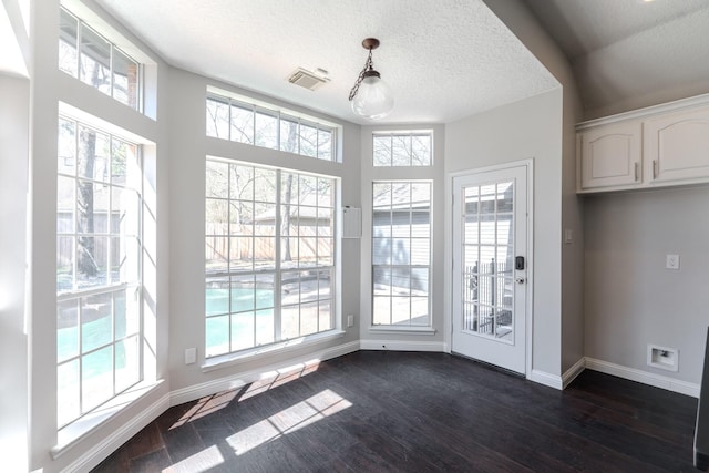 unfurnished dining area with dark wood-style floors, visible vents, baseboards, and a wealth of natural light