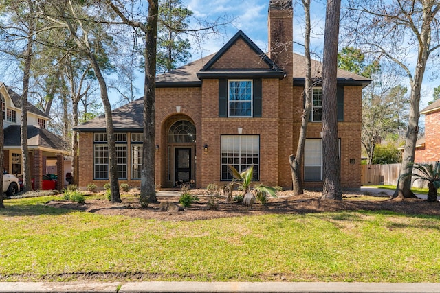 traditional-style house featuring a front yard, fence, and brick siding