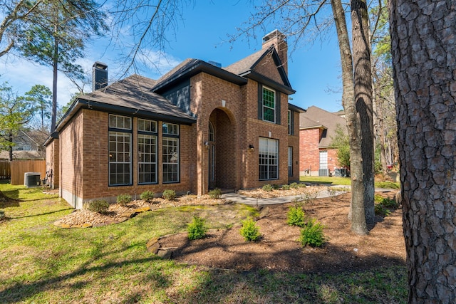 back of house with brick siding, fence, central AC, a lawn, and a chimney