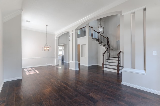 unfurnished living room with stairway, arched walkways, an inviting chandelier, and wood finished floors