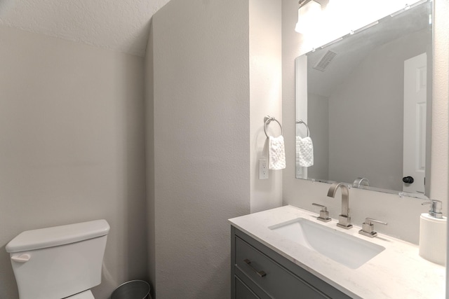 half bathroom featuring toilet, vanity, and a textured wall