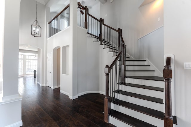 staircase with arched walkways, a high ceiling, baseboards, and hardwood / wood-style flooring