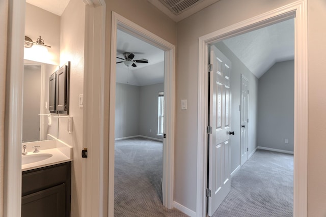 hallway featuring visible vents, light carpet, a sink, baseboards, and lofted ceiling