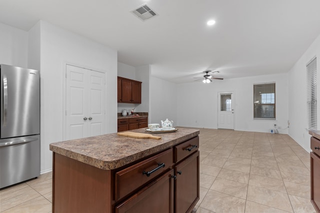 kitchen with light tile patterned floors, visible vents, ceiling fan, a kitchen island, and freestanding refrigerator