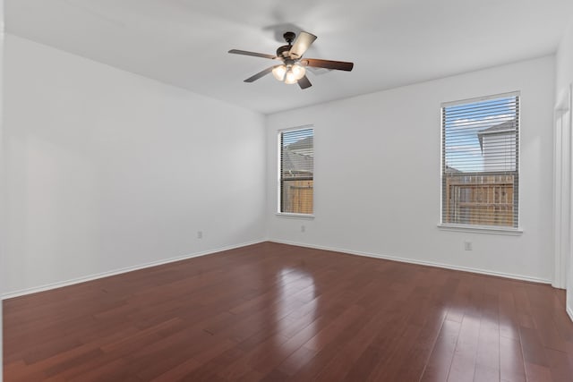 spare room featuring baseboards, dark wood finished floors, and a ceiling fan