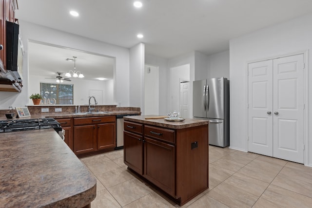 kitchen with light tile patterned floors, dark countertops, a kitchen island, appliances with stainless steel finishes, and a sink