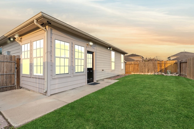 back of house at dusk featuring a yard, a patio, and fence