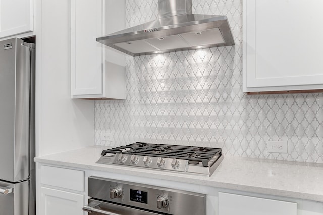 kitchen featuring white cabinets, appliances with stainless steel finishes, light stone countertops, wall chimney range hood, and backsplash