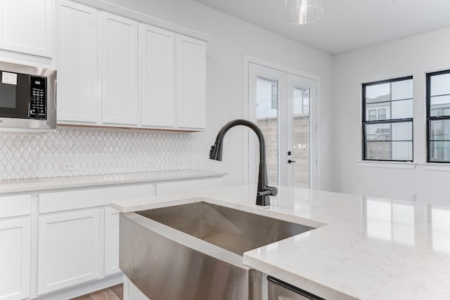 kitchen featuring tasteful backsplash, stainless steel microwave, white cabinets, a sink, and light stone countertops