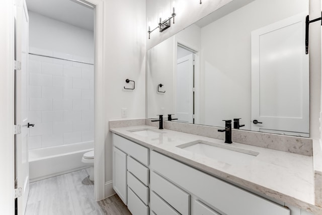 bathroom with toilet, double vanity,  shower combination, and a sink