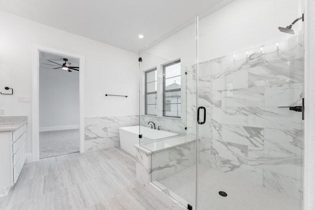 bathroom with a freestanding bath, a marble finish shower, vanity, and tile walls