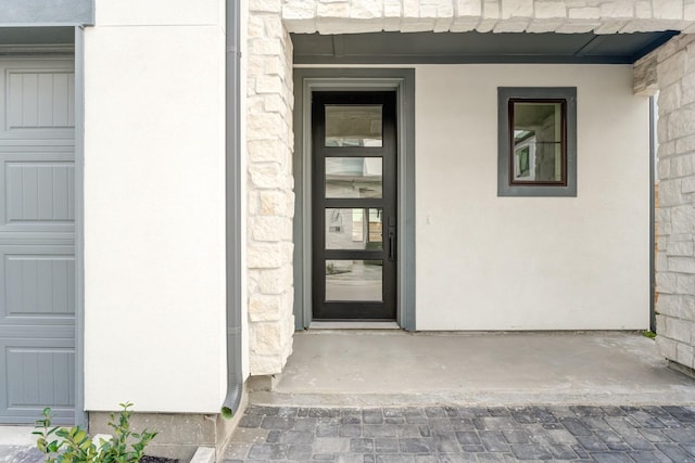 view of exterior entry with a garage, stone siding, and stucco siding