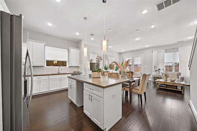 kitchen with a sink, open floor plan, stainless steel refrigerator with ice dispenser, decorative backsplash, and dark wood finished floors