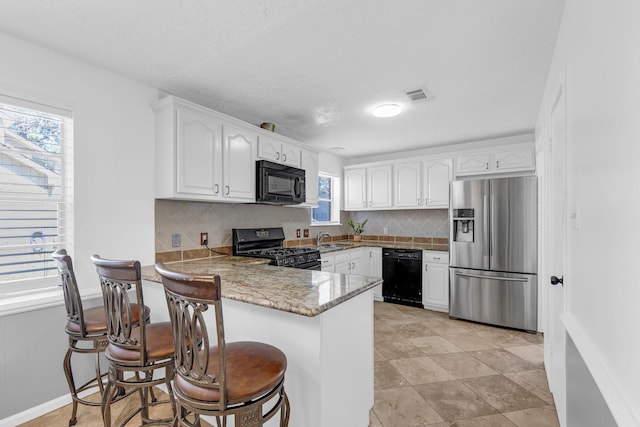 kitchen with visible vents, white cabinetry, a sink, a peninsula, and black appliances