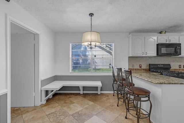 kitchen featuring light stone counters, pendant lighting, tasteful backsplash, white cabinetry, and black appliances