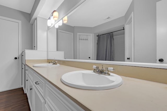 full bathroom with double vanity, visible vents, a sink, and wood finished floors