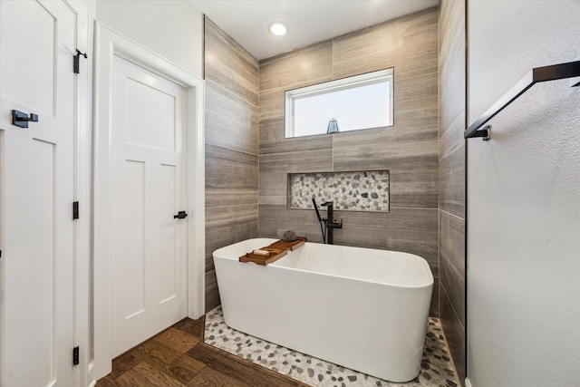 full bath featuring wood finished floors, tile walls, and a freestanding tub