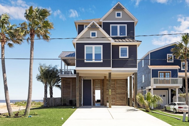 coastal inspired home featuring a standing seam roof, concrete driveway, a front yard, and metal roof