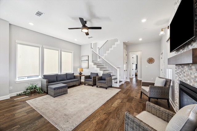 living room featuring visible vents, dark wood-type flooring, a stone fireplace, and stairs